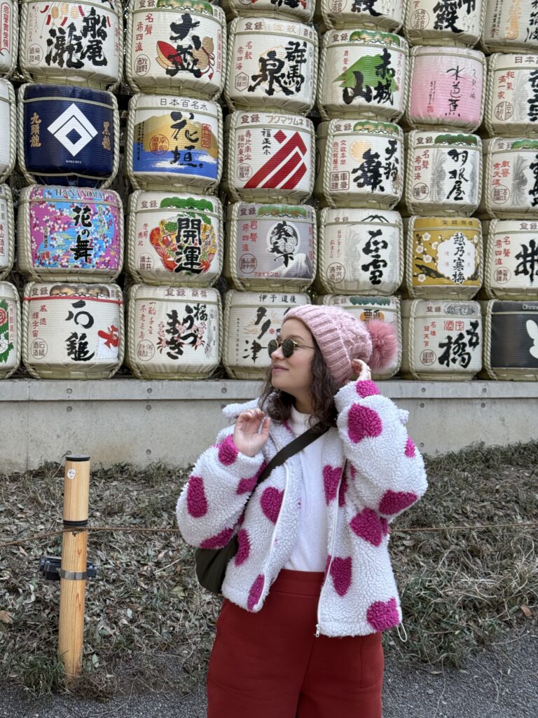 Mulher de gorro rosa em frente à parede de barris de saquê decorados do Santuário Meiji, em Tóquio
