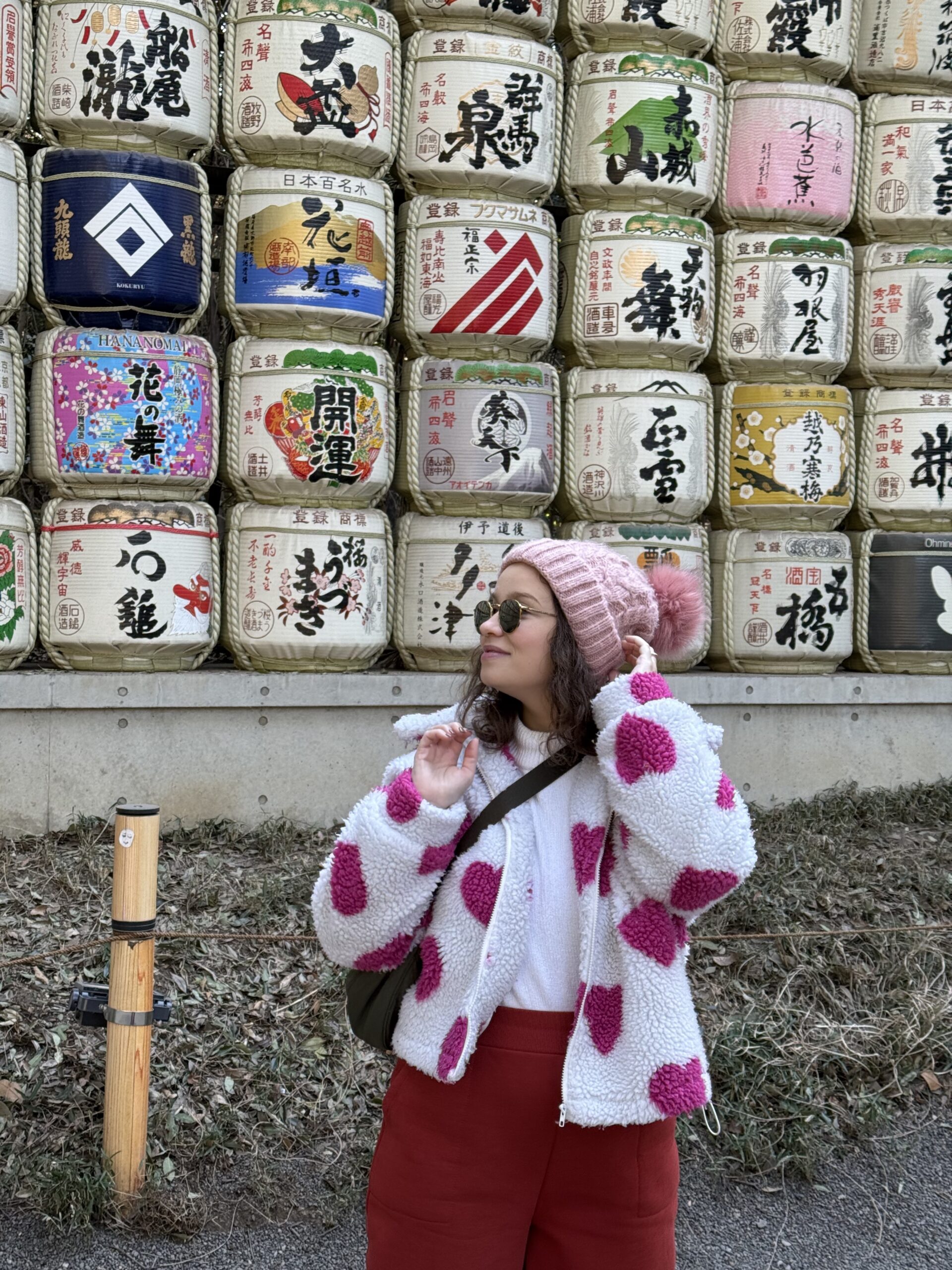 Mulher de gorro rosa em frente à parede de barris de saquê decorados do Santuário Meiji, em Tóquio