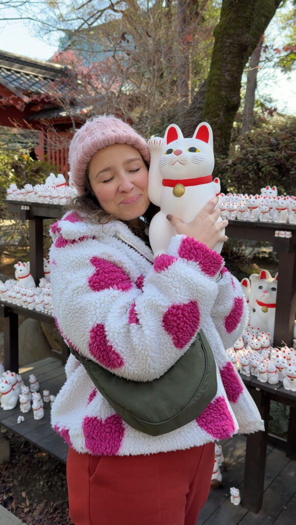 Mulher abraçando um maneki-neko grande diante das prateleiras com centenas de gatinhos da sorte no templo Gotokuji, em Tóquio