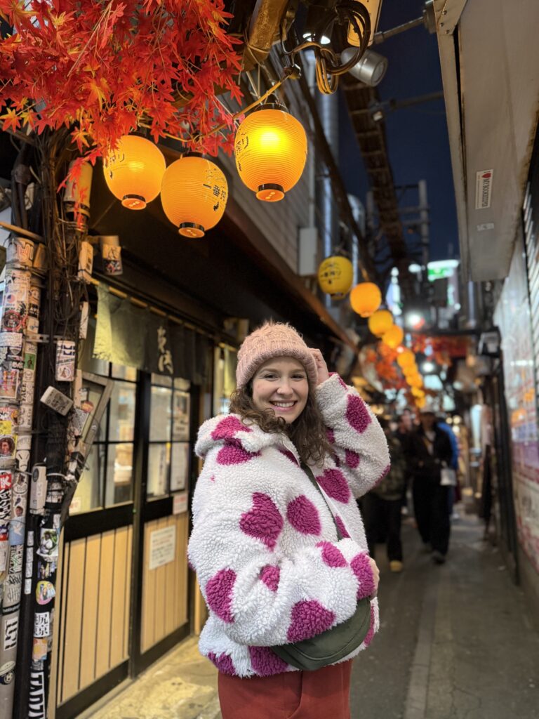 Mulher sorrindo em um beco estreito de izakayas iluminado por lanternas de papel, à noite, em Tóquio