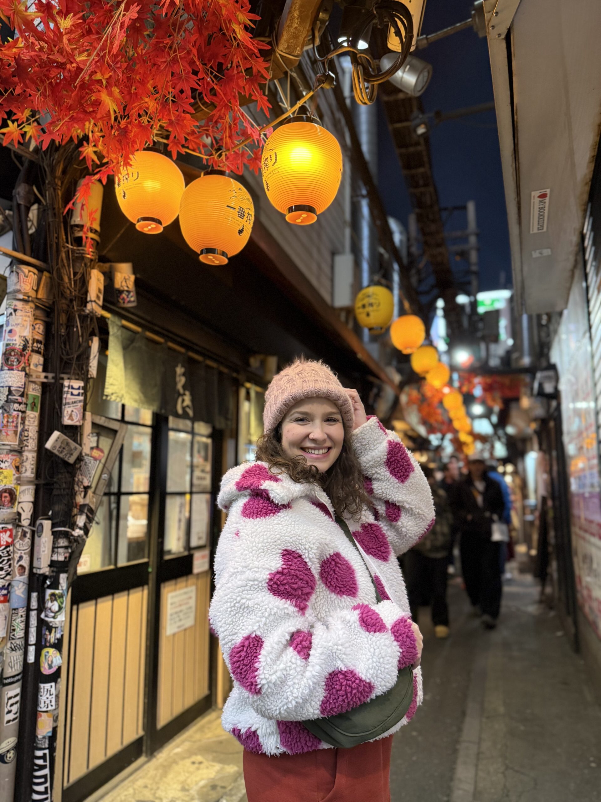 Mulher sorrindo em um beco estreito de izakayas iluminado por lanternas de papel, à noite, em Tóquio