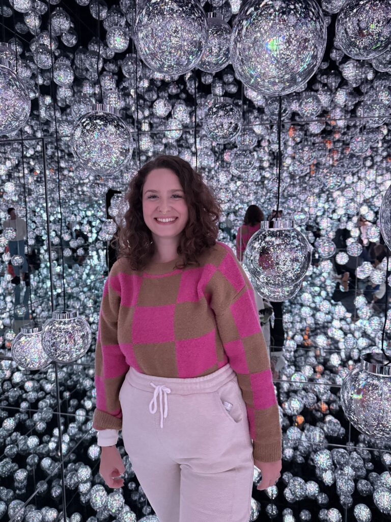 Mulher sorrindo dentro de sala de espelhos com centenas de esferas iluminadas em uma instalação do teamLab, em Tóquio