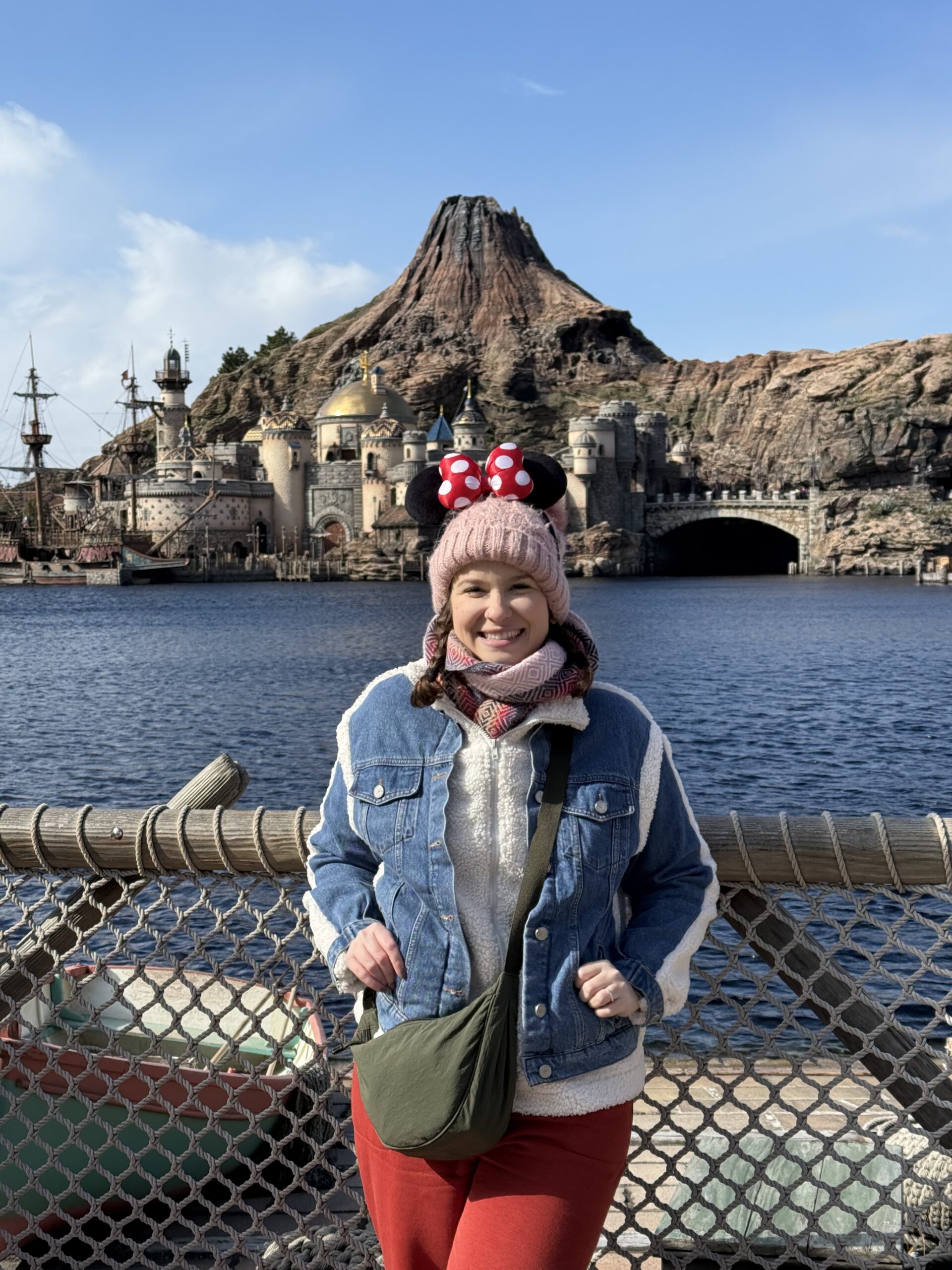 Mulher com orelhas da Minnie em frente ao vulcão Monte Prometheus e ao porto Mediterranean Harbor da Tokyo DisneySea