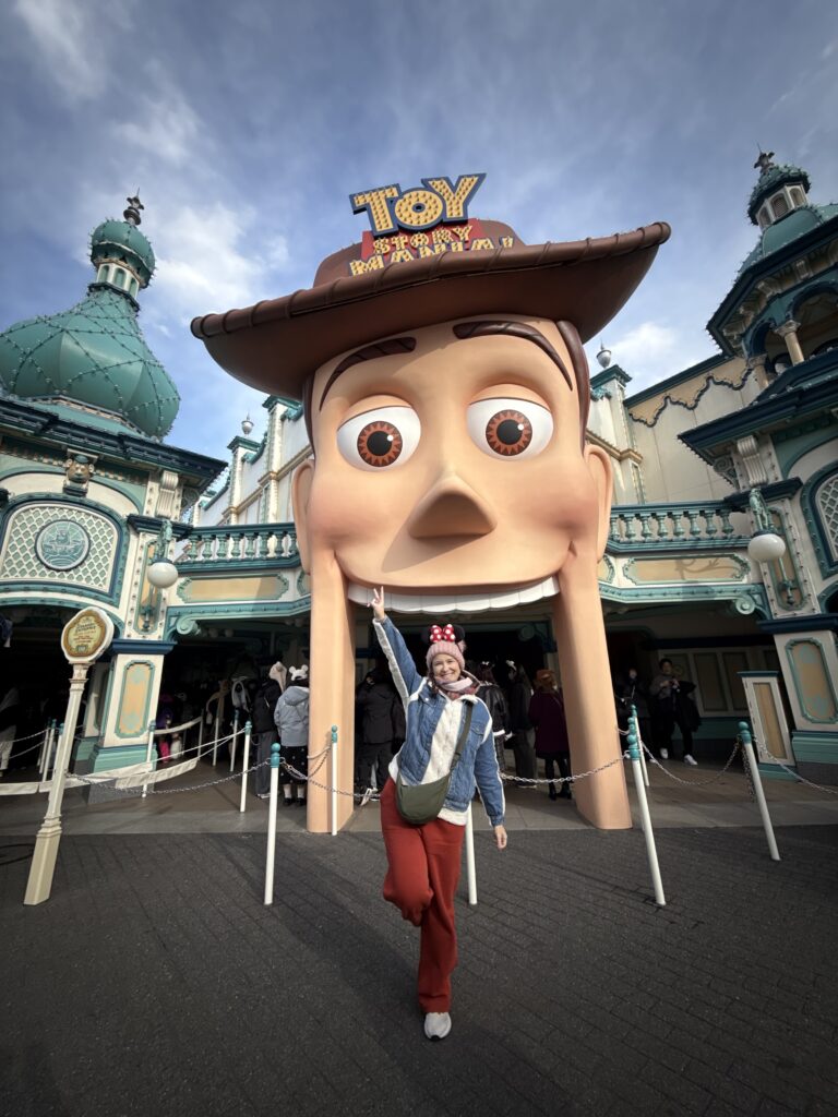 Mulher em frente à entrada da atração Toy Story Mania, com a cabeça gigante do Woody, na Tokyo DisneySea