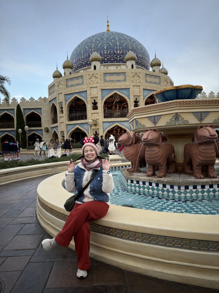 Mulher sentada na borda da fonte dos camelos em frente ao domo azul da área Arabian Coast, na Tokyo DisneySea
