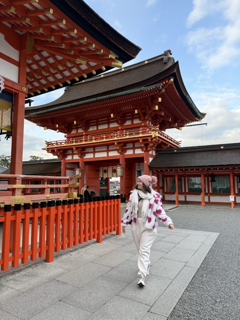 Mulher caminhando em frente ao prédio principal laranja do santuário Fushimi Inari Taisha, em Kyoto