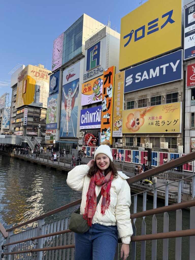 Mulher no canal de Dotonbori com os letreiros luminosos e o painel do Glico ao fundo, em Osaka