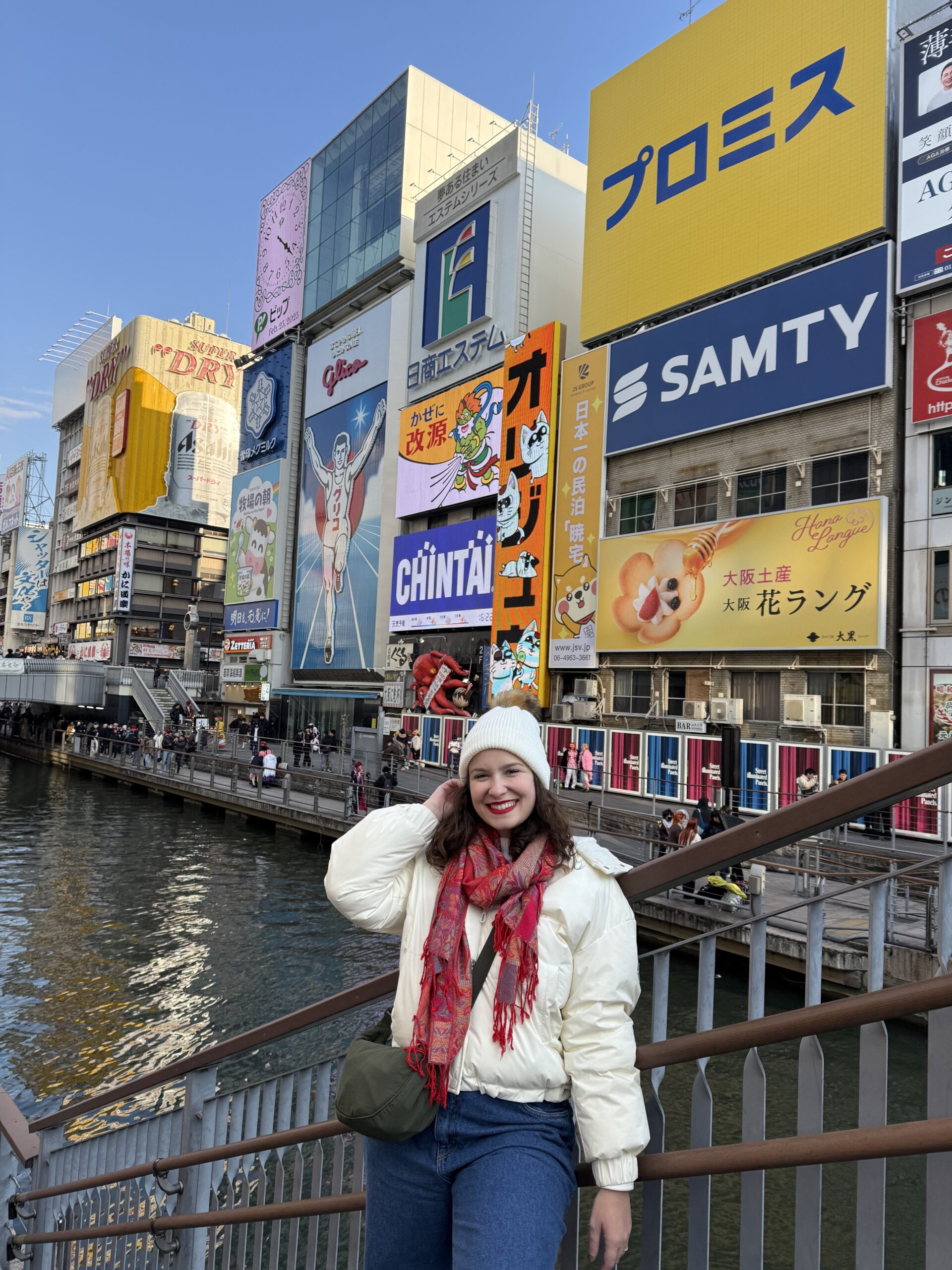 Mulher no canal de Dotonbori com os letreiros luminosos e o painel do Glico ao fundo, em Osaka