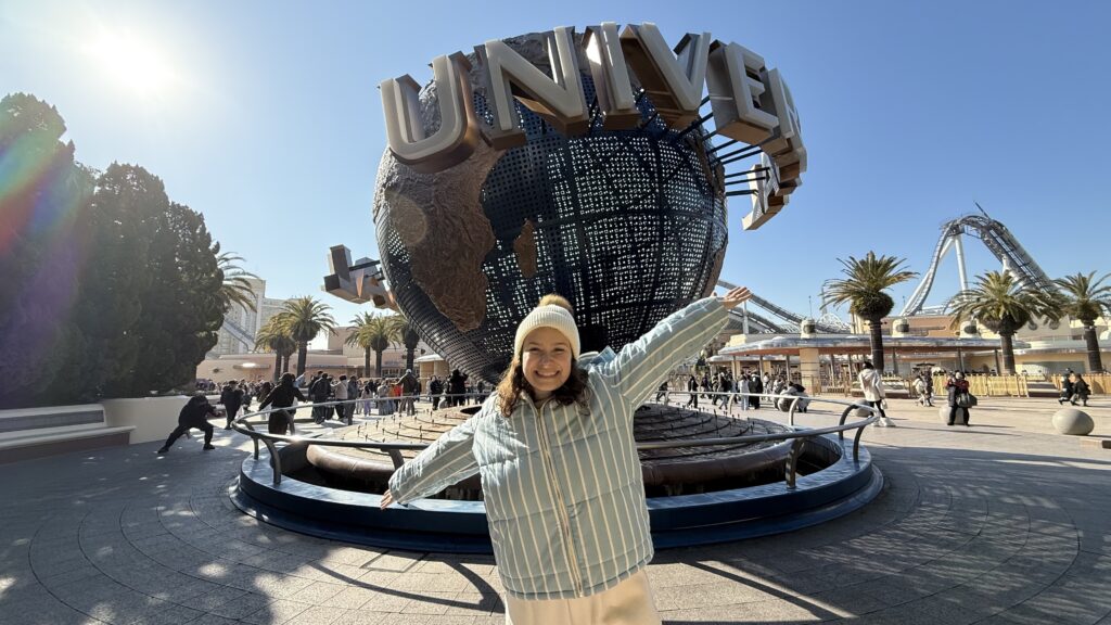 Mulher em frente ao globo do Universal Studios Japan com a montanha-russa ao fundo, em Osaka
