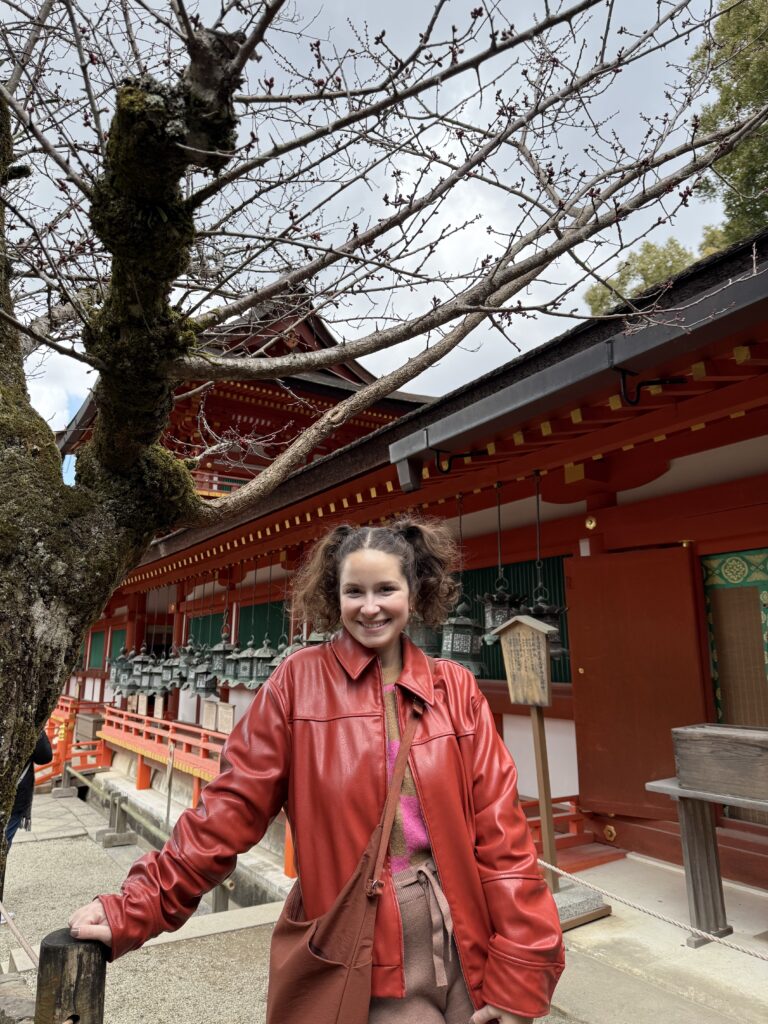 Mulher em frente ao corredor vermelho do santuário Kasuga Taisha, com fileiras de lanternas de bronze, em Nara