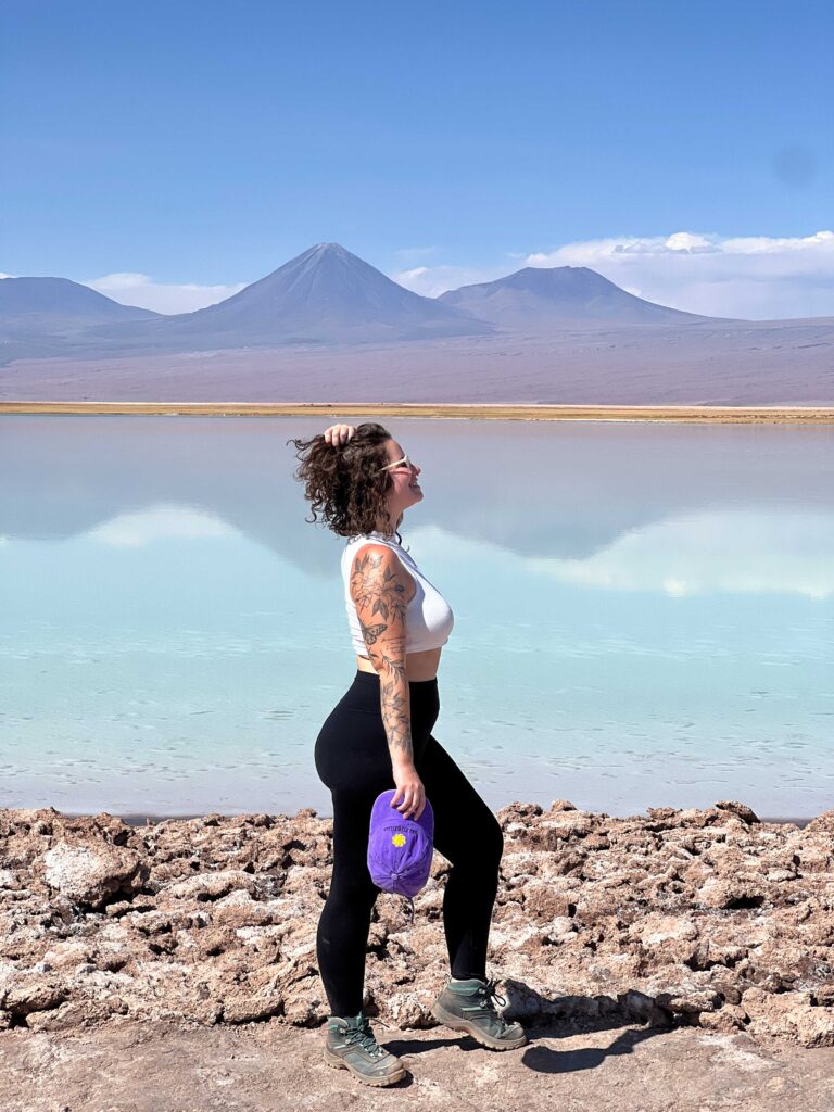 Mulher na margem de uma lagoa de água turquesa com vulcões ao fundo no deserto do Atacama, Chile