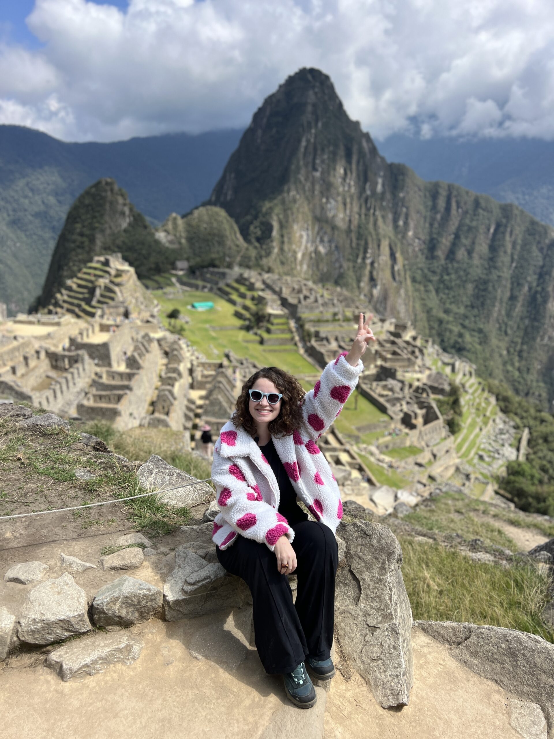 Mulher sentada no mirante de Machu Picchu com a cidadela inca e o Huayna Picchu ao fundo