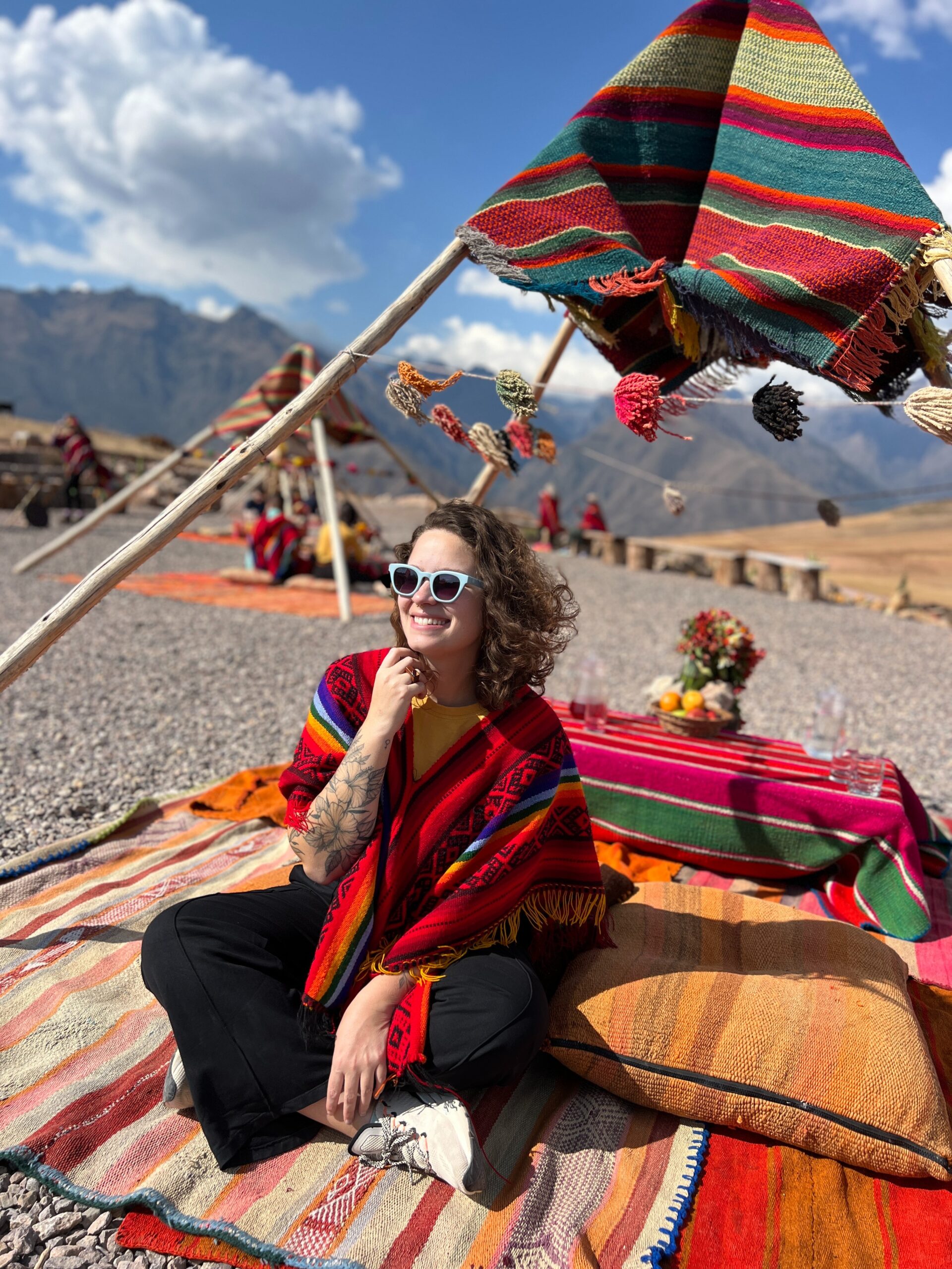 Viajante de poncho andino vermelho sentada em manta colorida durante piquenique com vista para as montanhas perto de Cusco