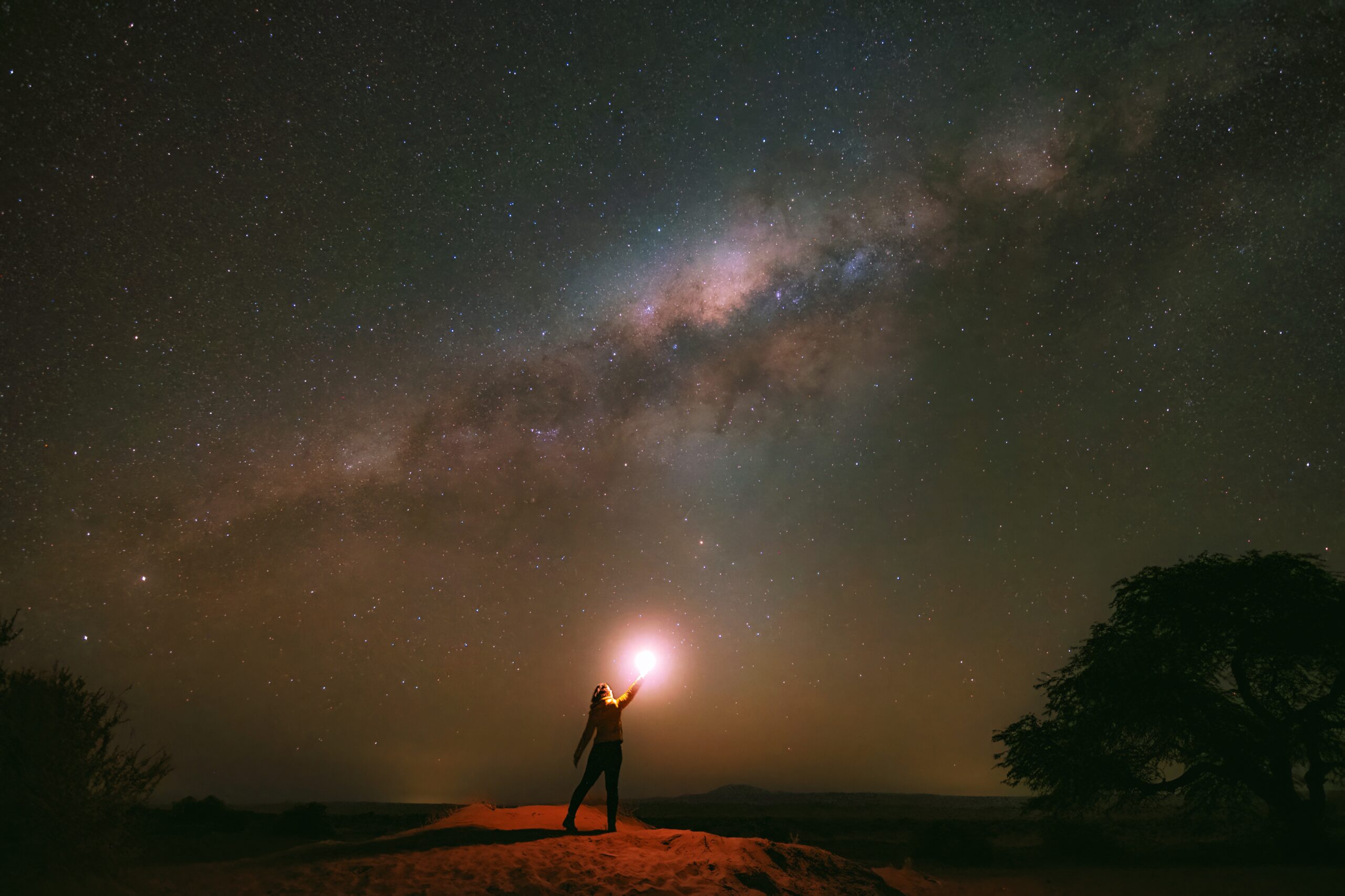 Mulher apontando uma lanterna para a Via Láctea no céu noturno do deserto do Atacama