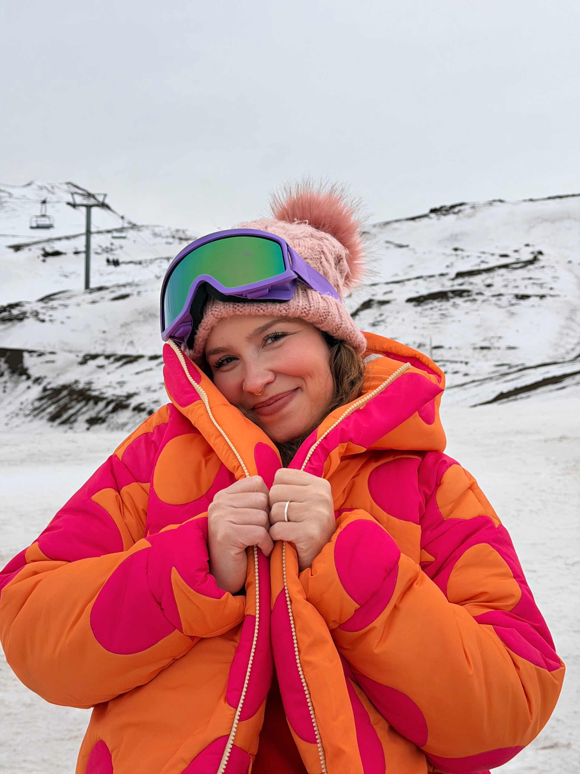 Mulher sorrindo com óculos de esqui e gorro na neve do Valle Nevado, no Chile
