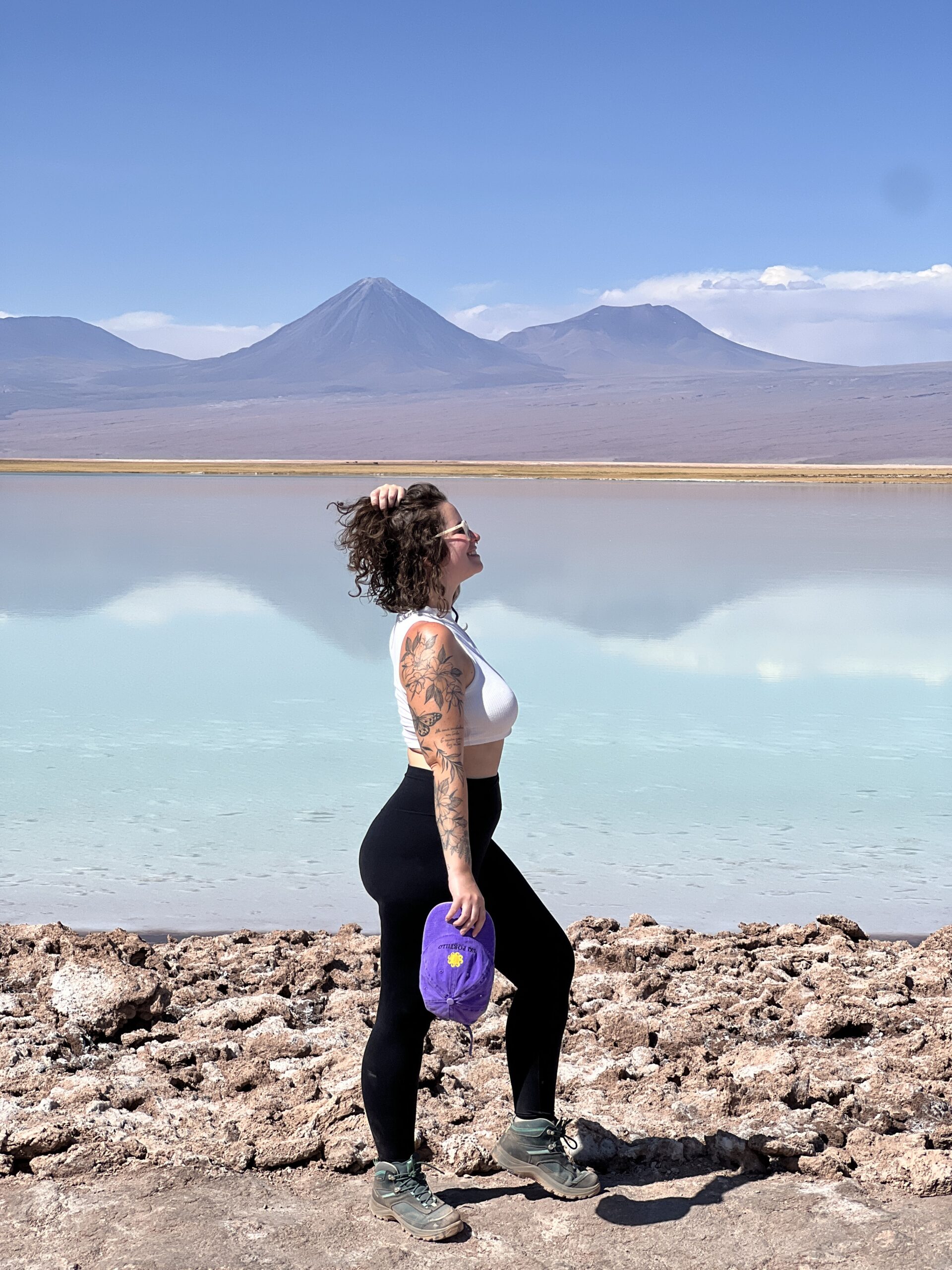 Mulher diante da lagoa salgada do Atacama com vulcão refletido na água