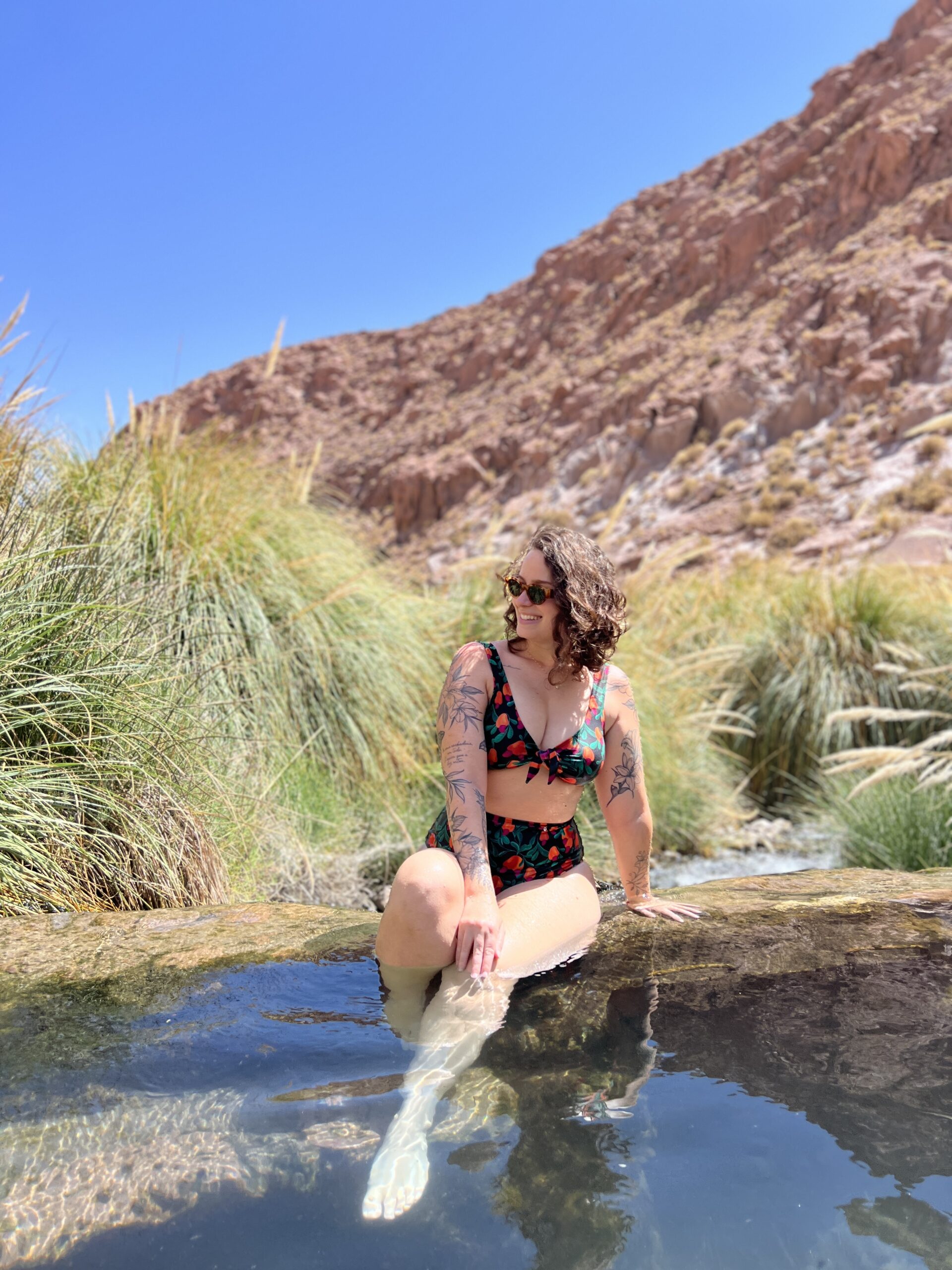 Pés na água morna das Termas de Puritama, cercada por vegetação, Atacama