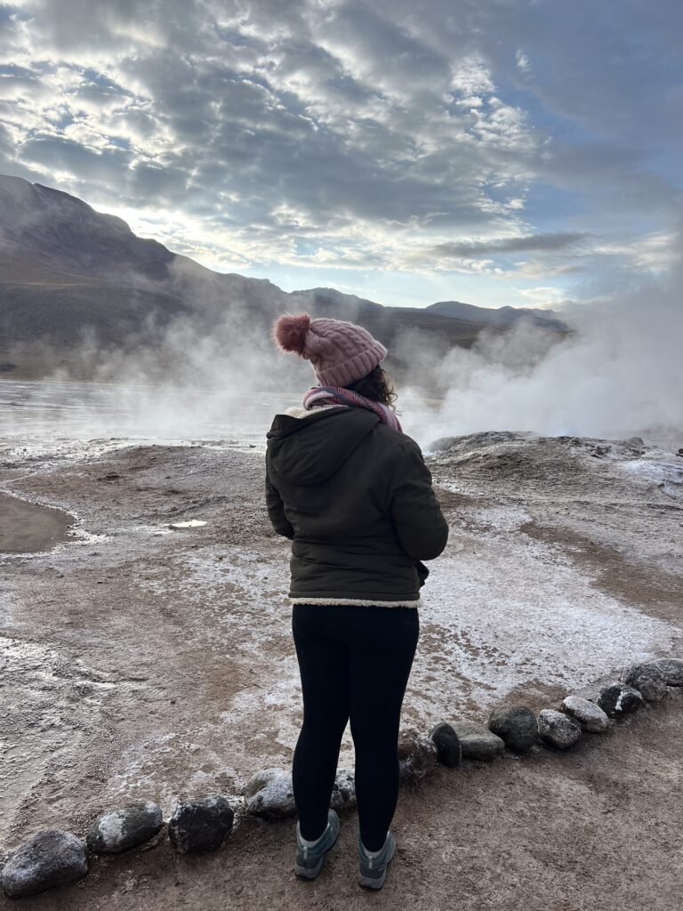 Mulher de costas observando o vapor dos Geiseres del Tatio no frio do amanhecer