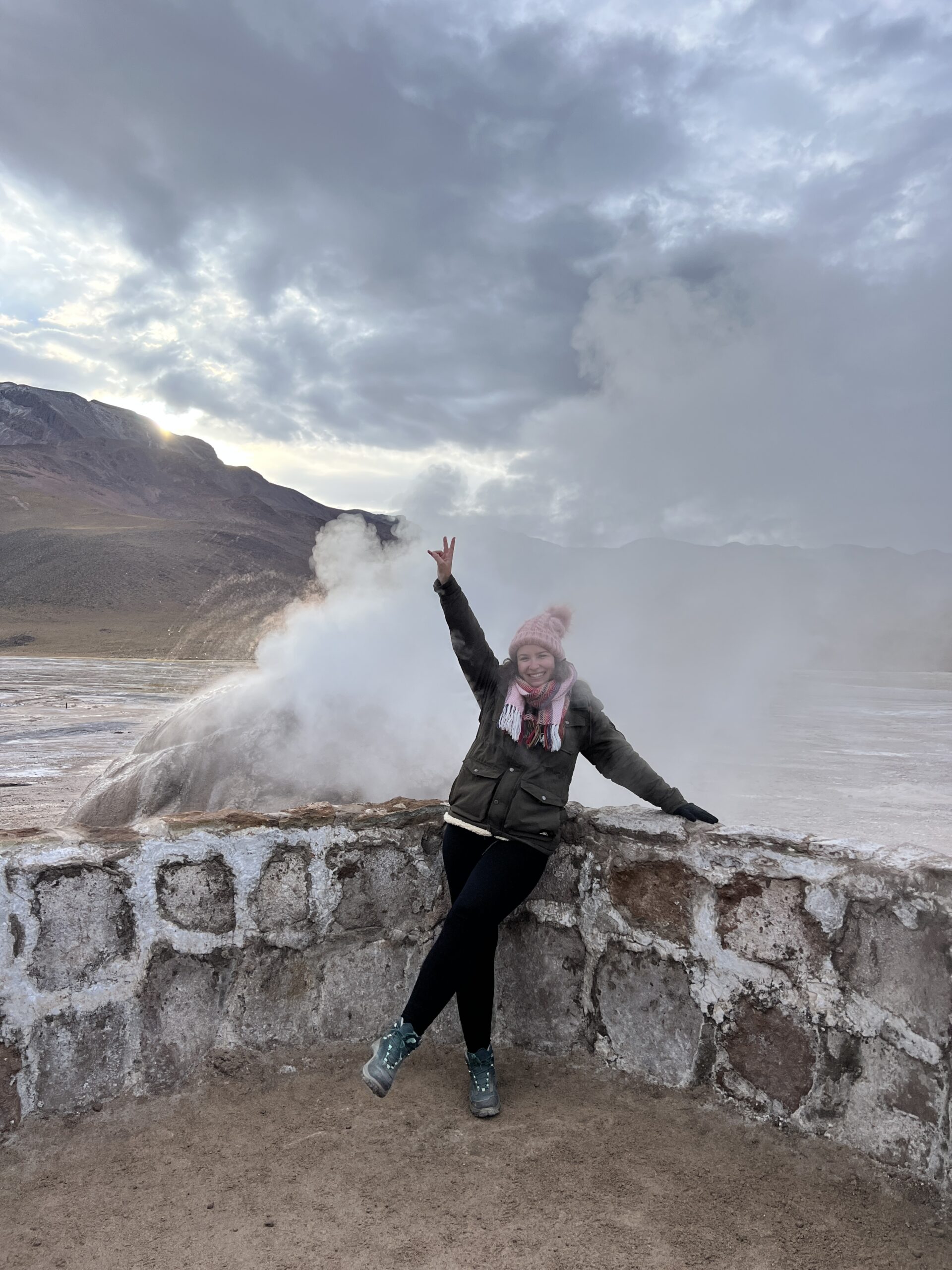 Mulher de braços abertos ao lado de uma fumarola dos Geiseres del Tatio, Atacama