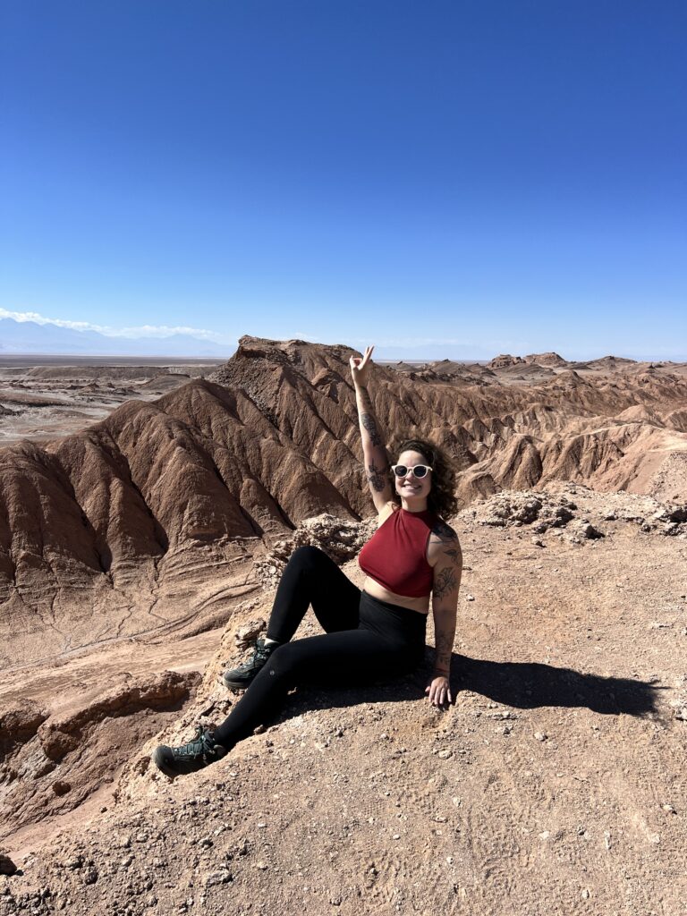 Mulher sentada diante das rochas avermelhadas do Valle de Marte, no Atacama