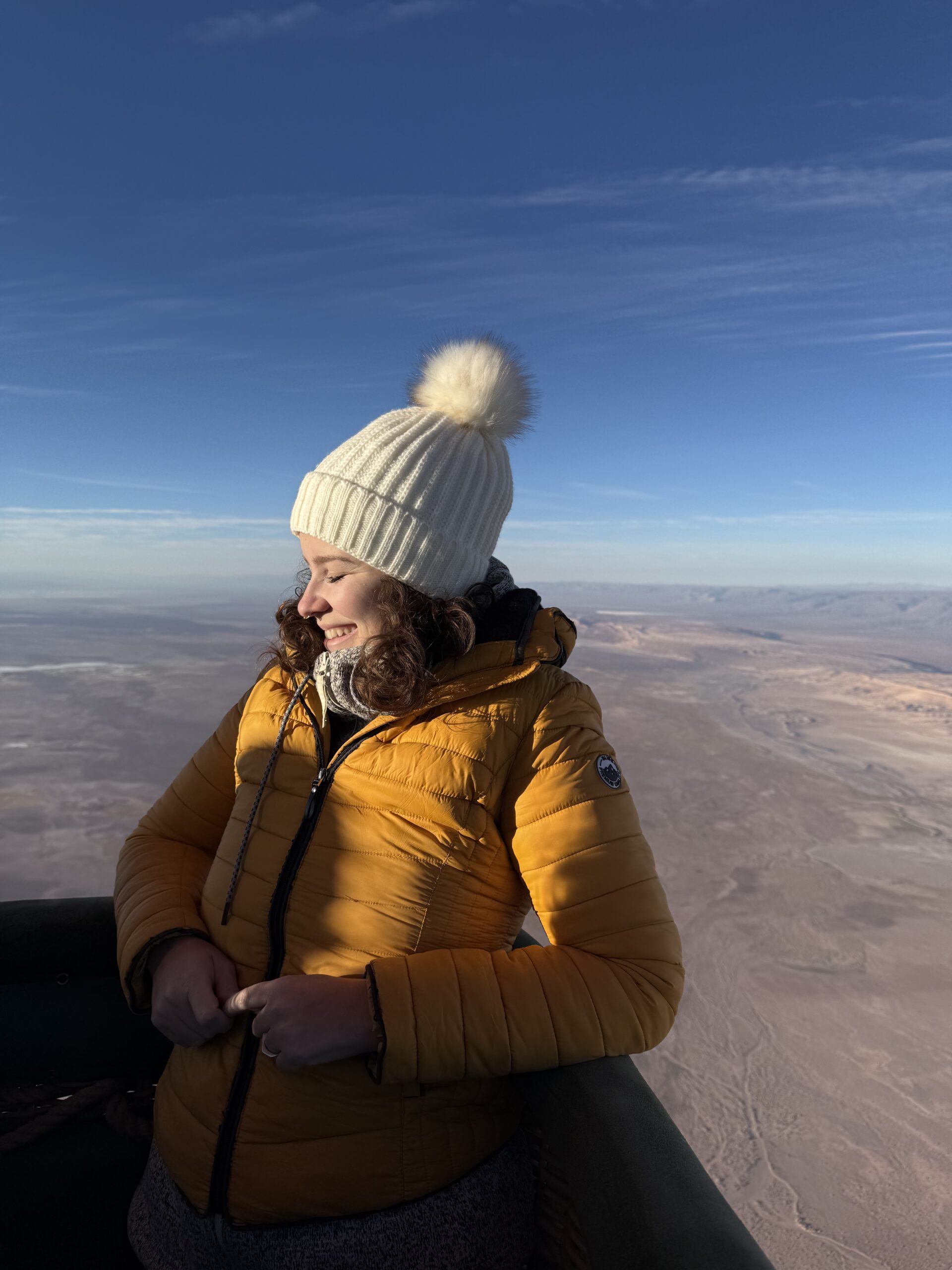 Mulher de casaco e gorro dentro do cesto do balão sobrevoando o deserto do Atacama