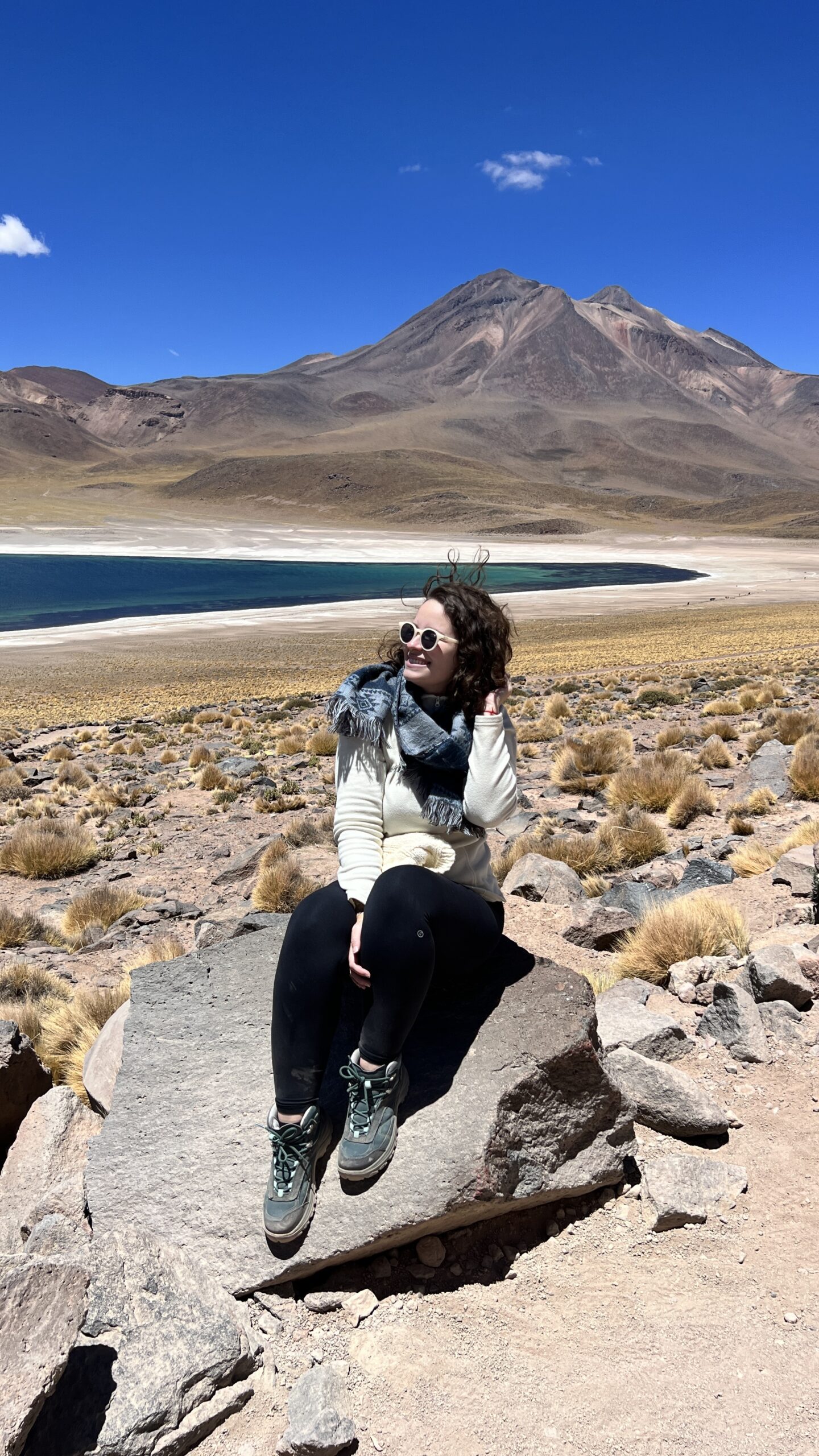 Mulher sentada em pedra com a Laguna Miñiques ao fundo, Atacama