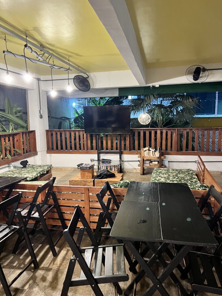 Espaço coberto com mesas no hostel onde dormi em Manaus