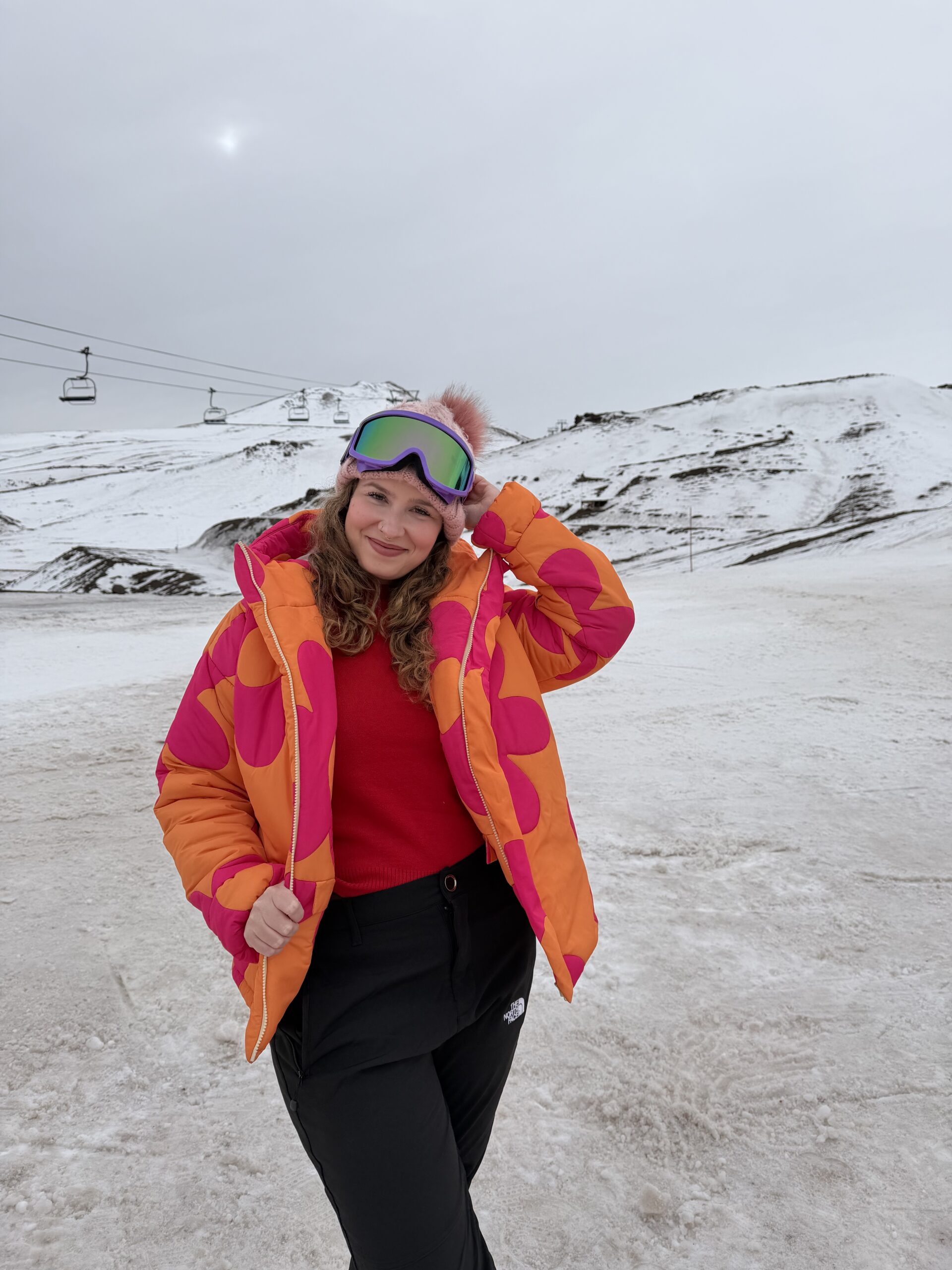 Mulher de casaco laranja na neve do Valle Nevado, no Chile, com a montanha ao fundo